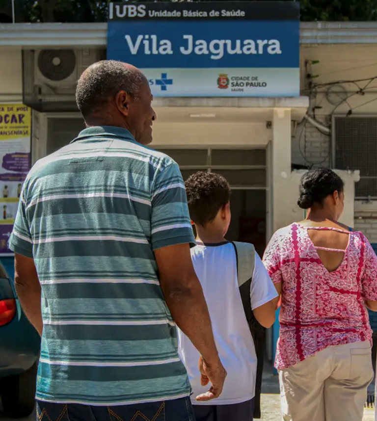 Uma mulher, um homem e uma criança caminham em direção à entrada da Unidade Básica de Saúde Vila Jaguara.